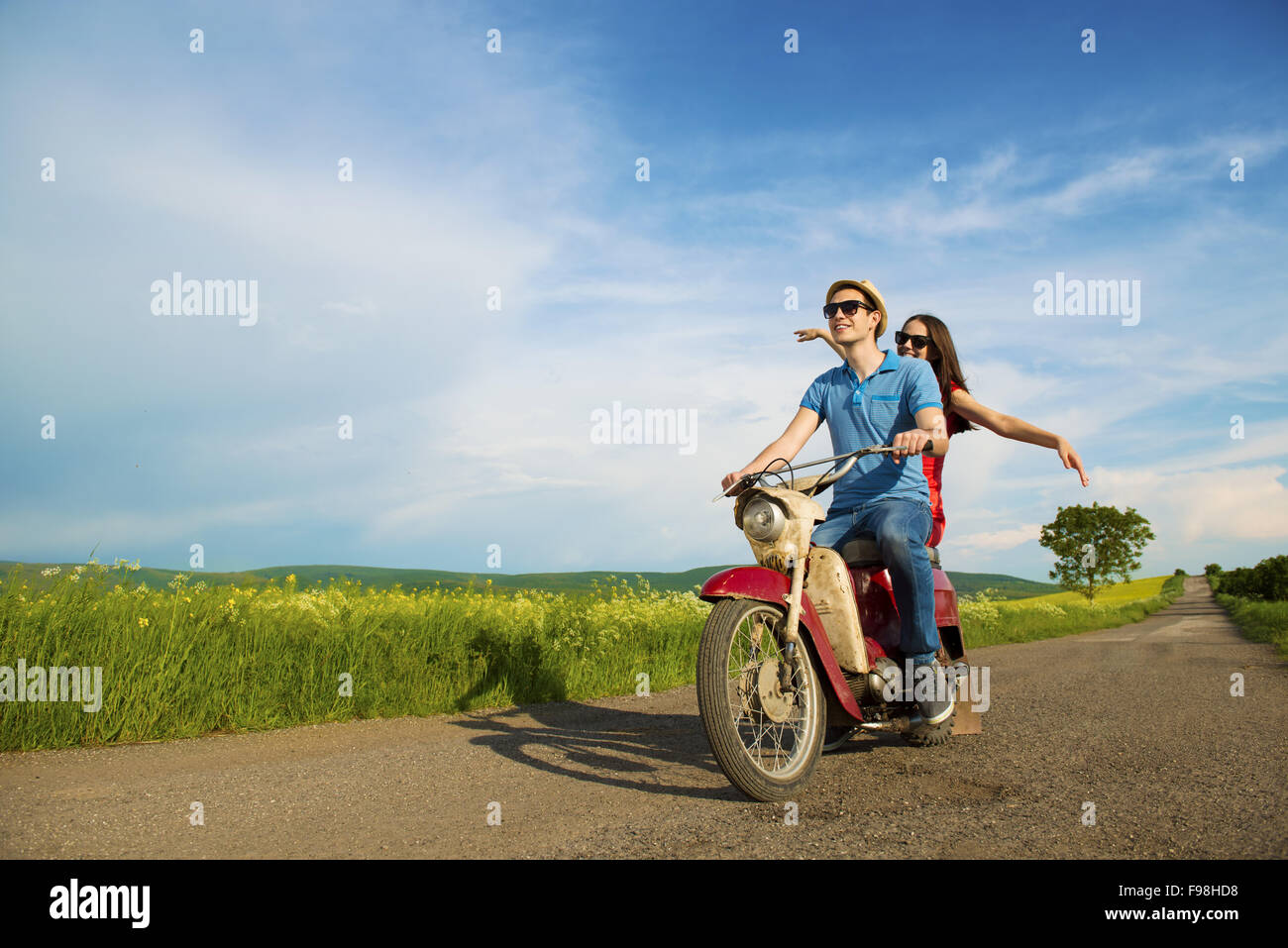 Joven pareja feliz en el amor sobre la conducción de motos togetger retro y gustando el viaje en campo verde Foto de stock