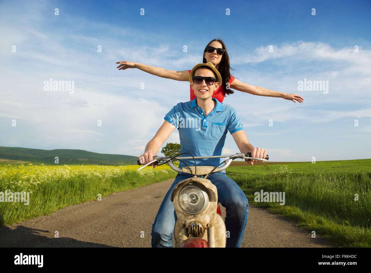 Joven pareja feliz en el amor sobre la conducción de motos togetger retro y gustando el viaje en campo verde Foto de stock