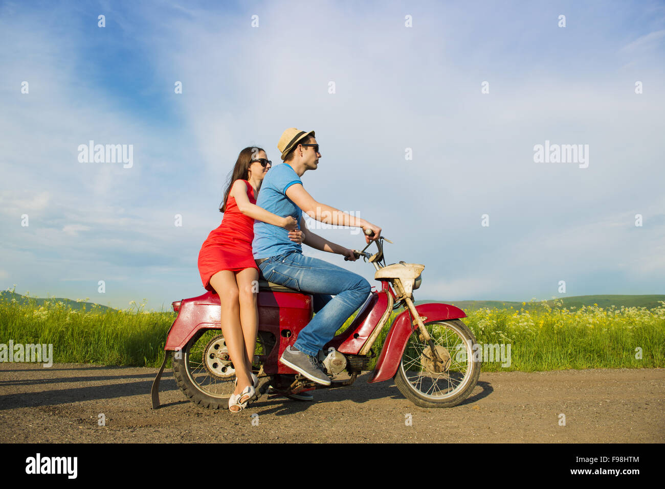 Joven pareja feliz en el amor sobre la conducción de motos togetger retro y gustando el viaje en campo verde Foto de stock