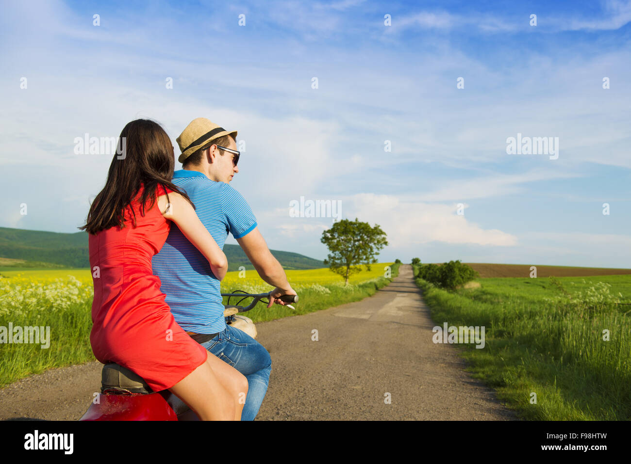 Joven pareja feliz en el amor sobre la conducción de motos togetger retro y gustando el viaje en campo verde Foto de stock