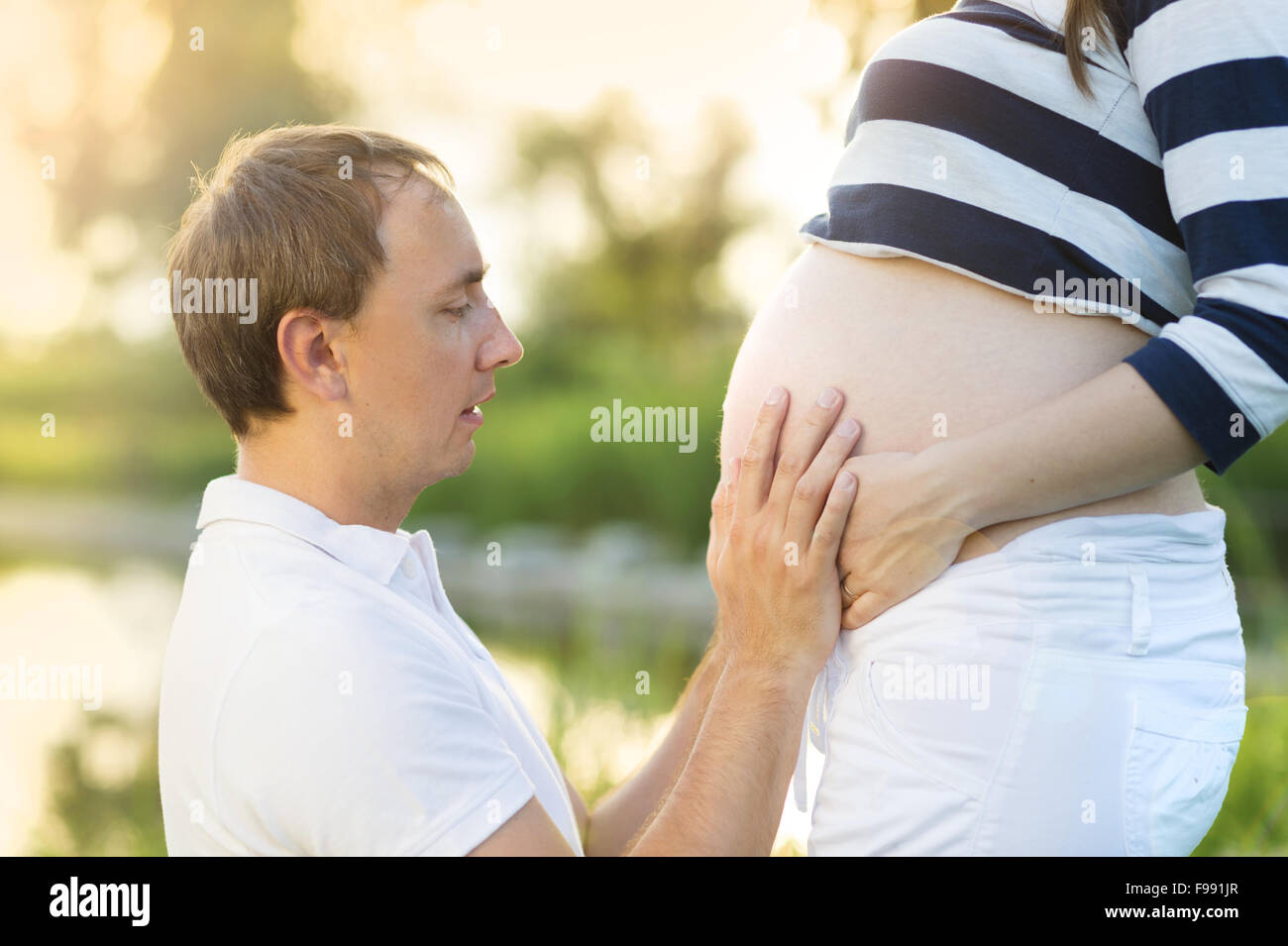 El hombre es besar el vientre de la mujer embarazada en la naturaleza Foto de stock