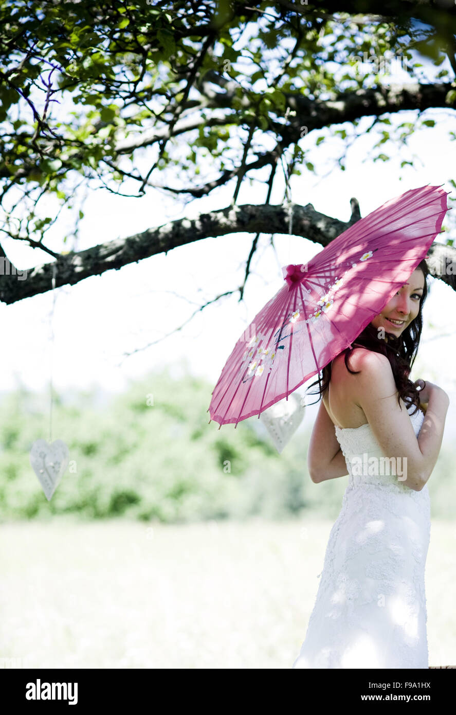 Novia vestido blanco con sombrilla posando en la pradera Foto de stock