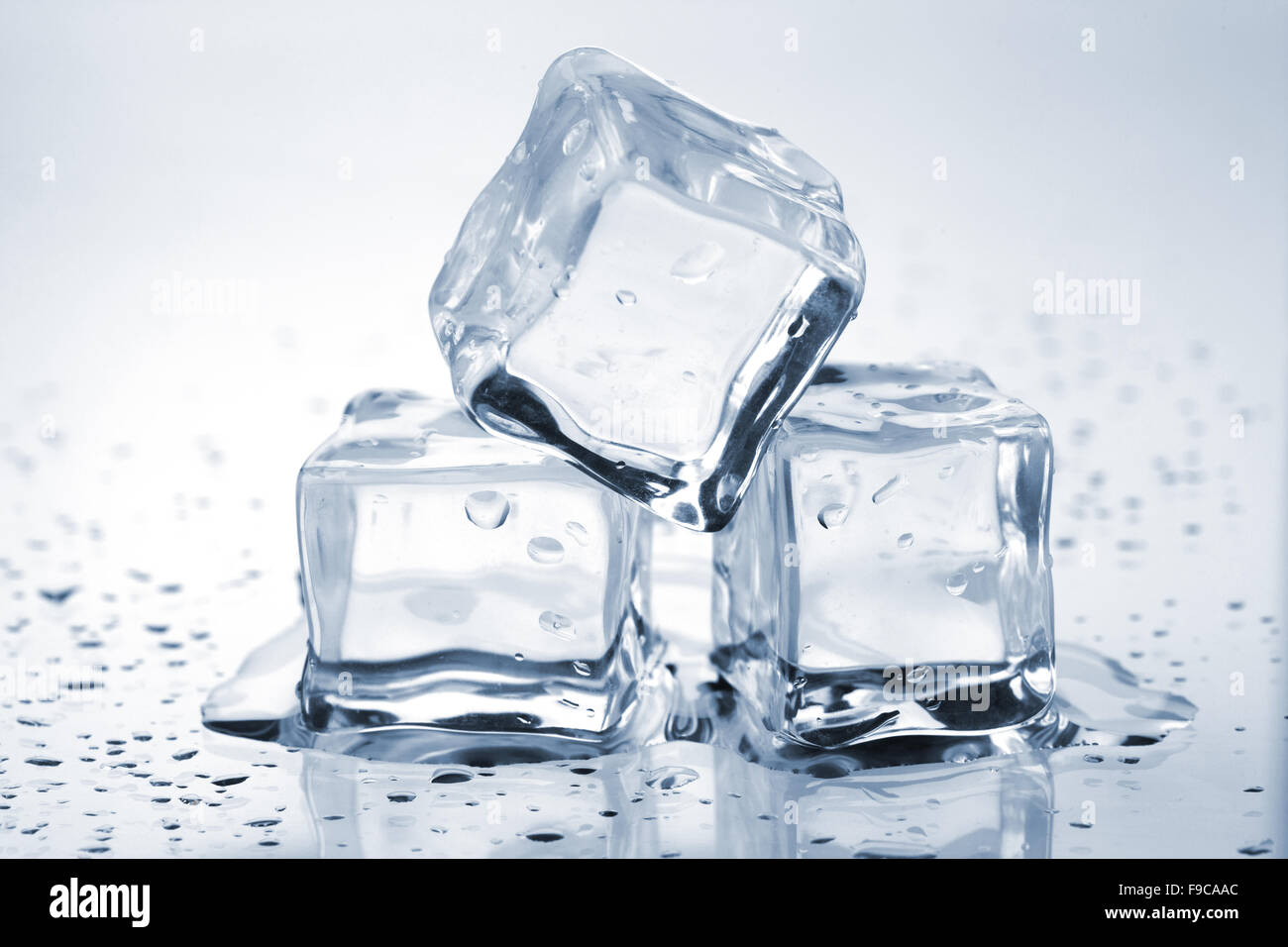 Tres cubos de hielo derritiéndose sobre una mesa de cristal Foto de stock