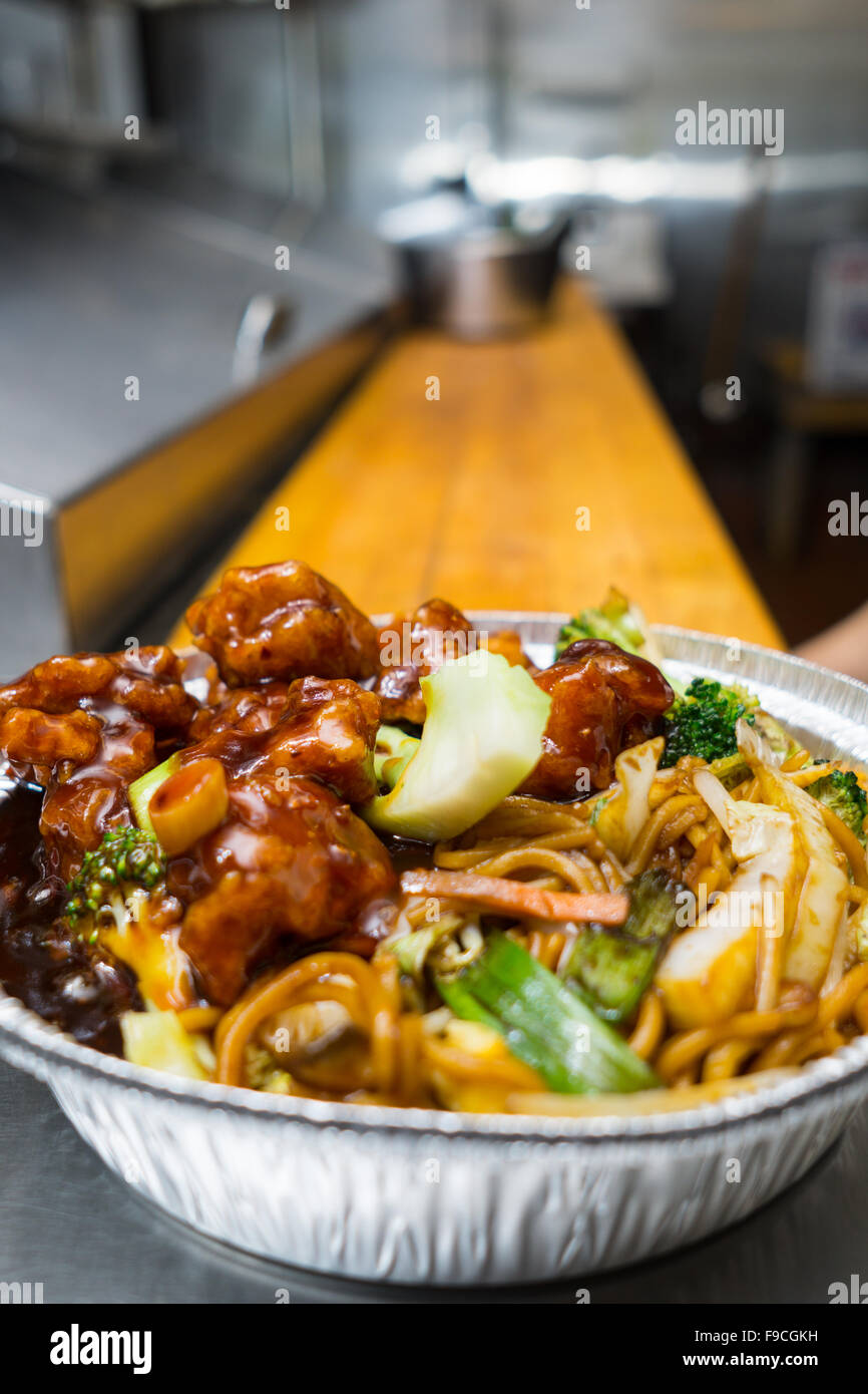 Plato popular chino el pollo del general tso en la mesa de la cocina en un saque el recipiente de lámina Foto de stock