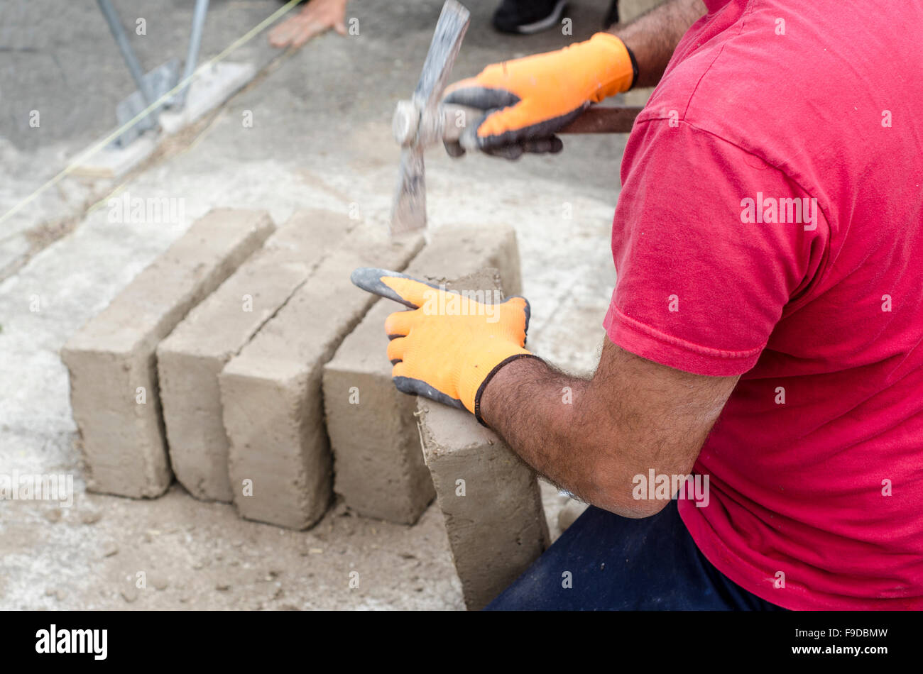 Albañil trabajando con ladrillos de barro para la construcción de un muro. Sitio en construcción Foto de stock