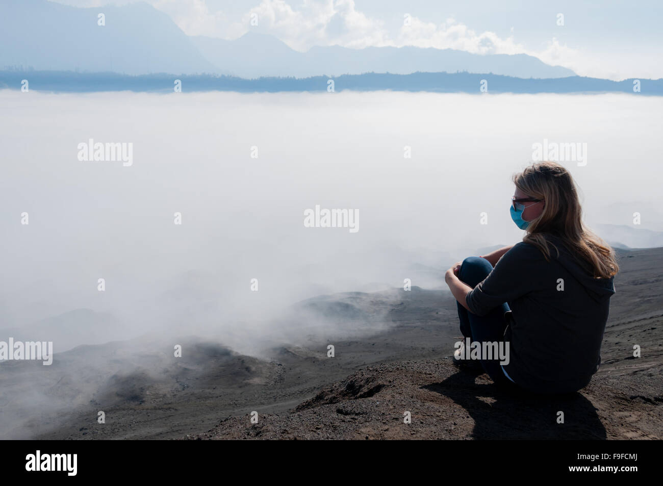 Mujer rubia descansando en la cima de la montaña viendo niebla de humo y niebla Foto de stock