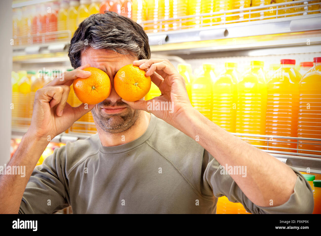 Hombre delante de la nevera con filas de botellas de zumo en un  supermercado que cubre sus ojos con dos naranjas Fotografía de stock - Alamy