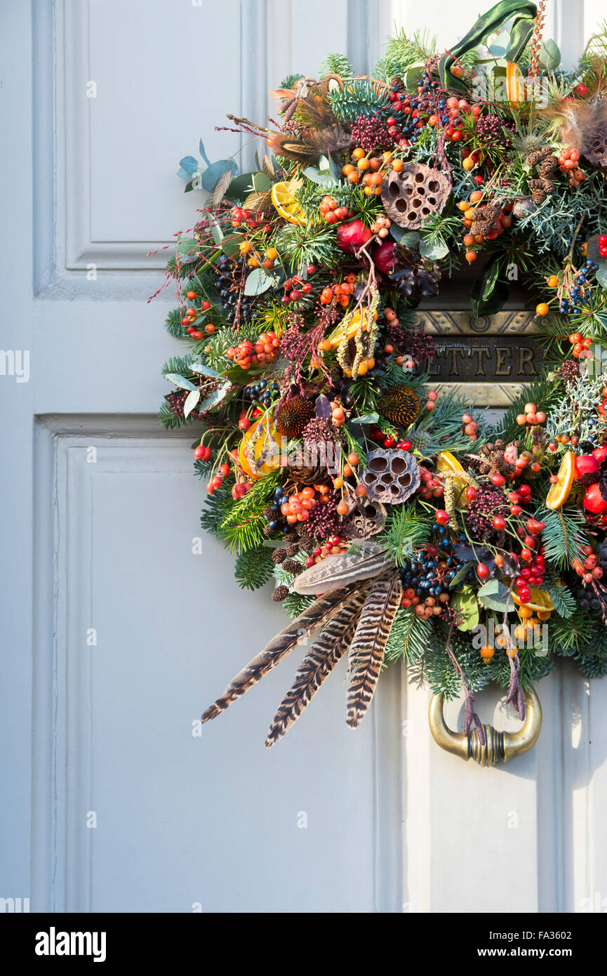 Navidad Berry, follaje, frutas y corona de plumas en la puerta de madera. Cotswolds, Inglaterra Foto de stock