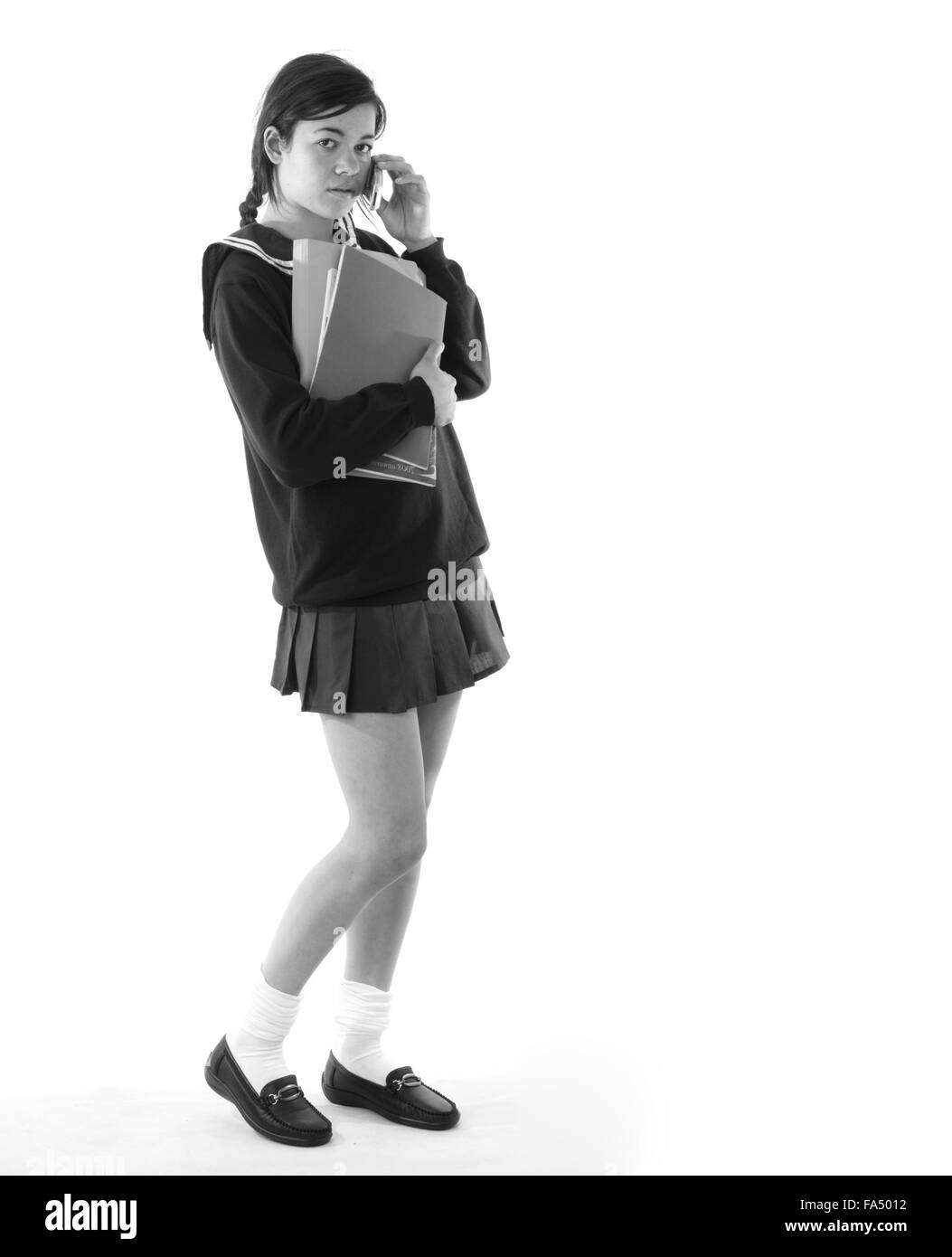 Colegiala en su celular llevando sus libros escolares, vestida con una minifalda muy corta Foto de stock