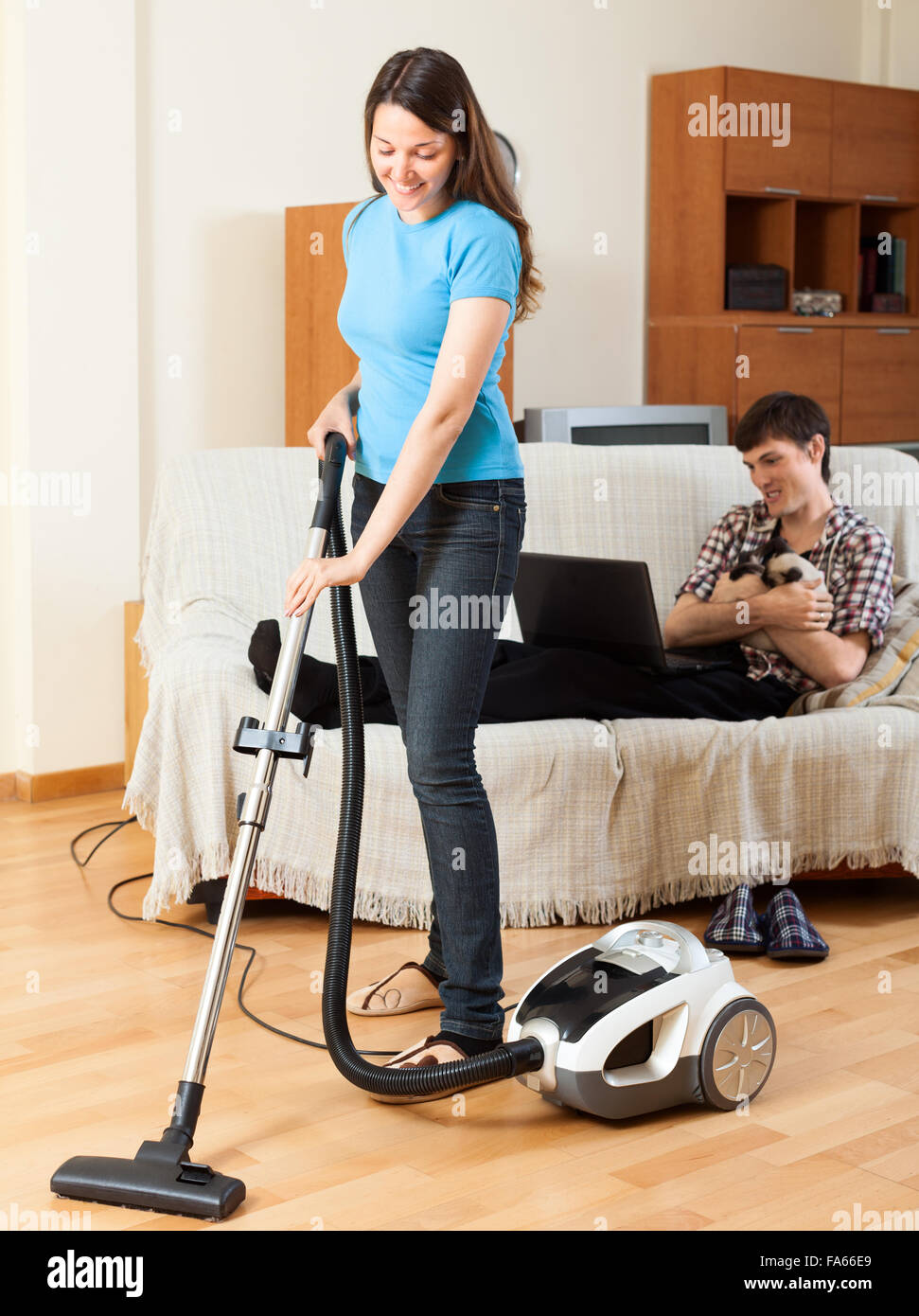 Chica haciendo limpieza en casa mientras el hombre con el portátil apoyado  sobre un sofá Fotografía de stock - Alamy