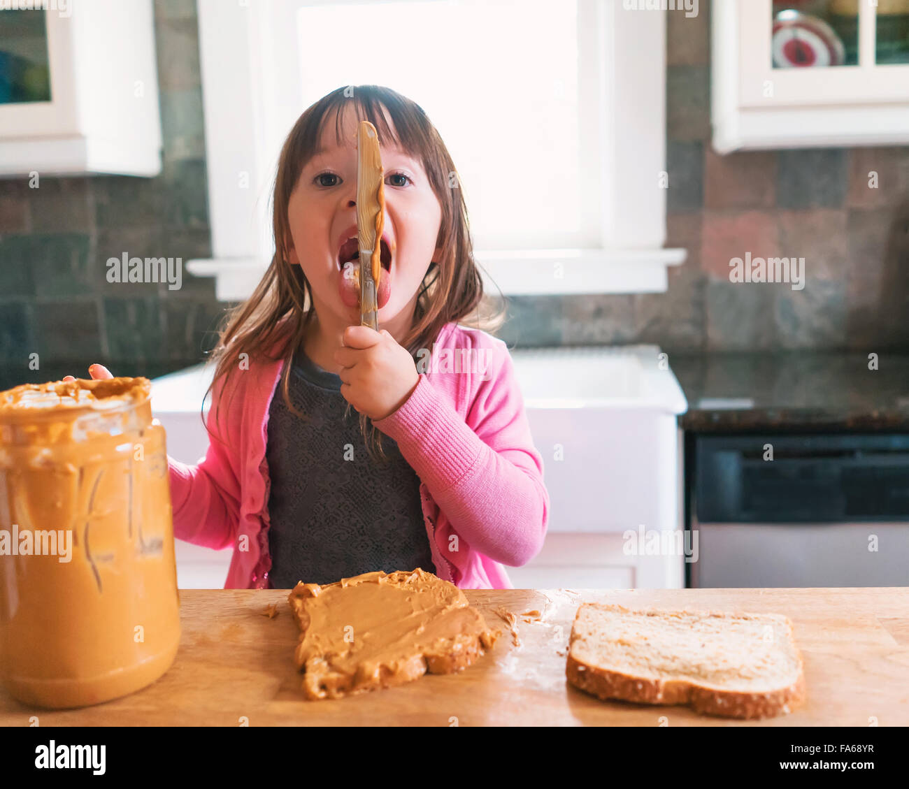 Chica haciendo un sándwich de mantequilla de maní, lamiendo la cuchilla Foto de stock