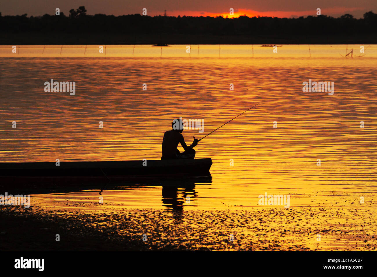Silueta hombre sentado en un barco de pesca al atardecer Foto de stock