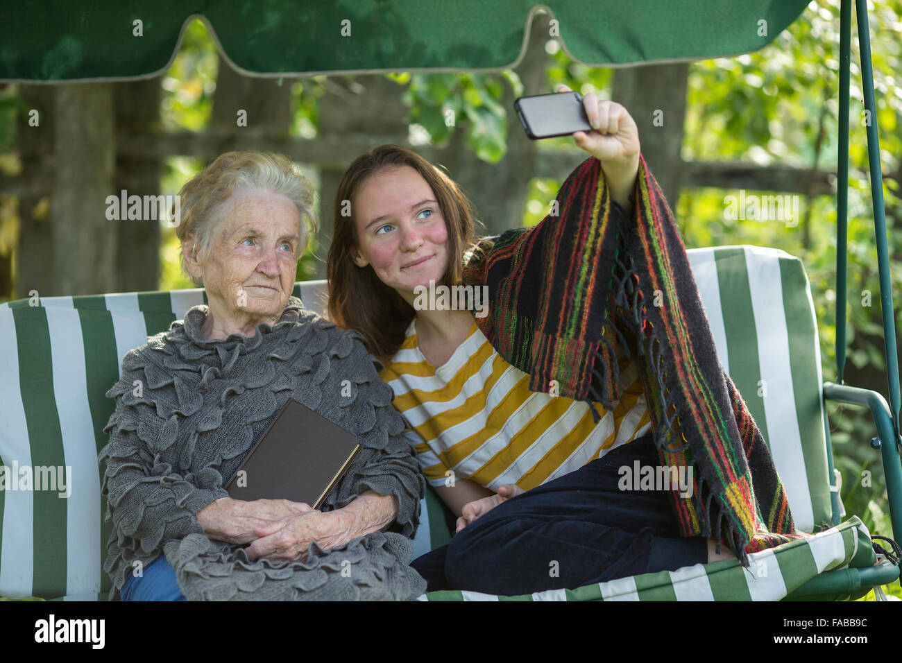 La muchacha sentada en la hamaca con la abuela y hace selfie. Foto de stock