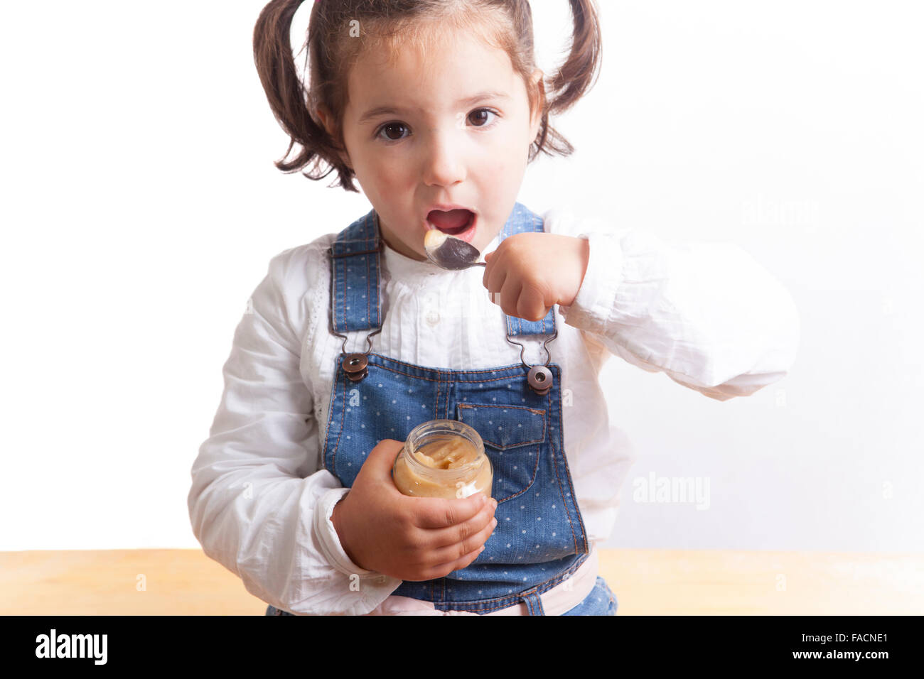 Retrato de niña alegre comer una fruta jarra de alimento para bebé. Aislado sobre fondo blanco. Foto de stock