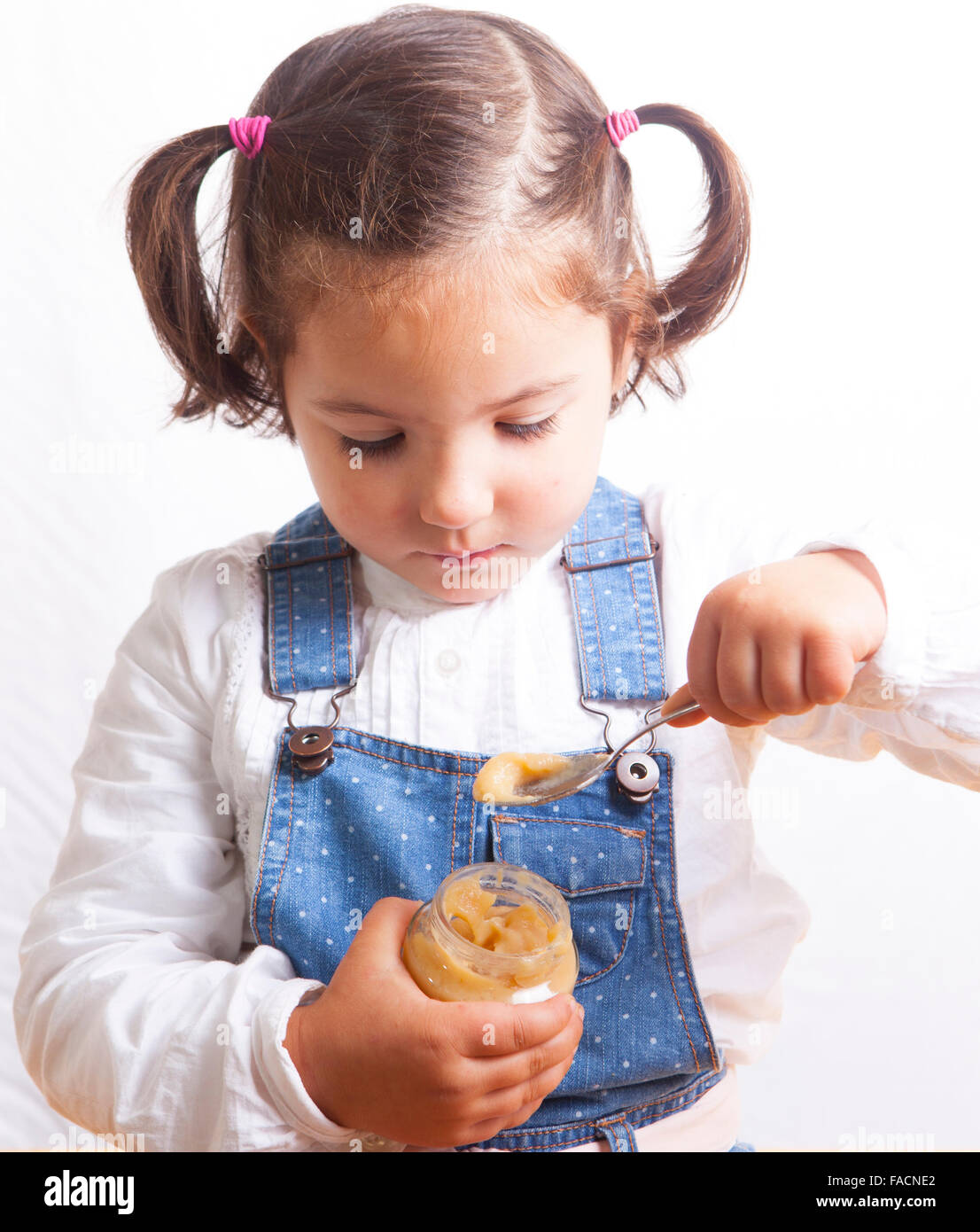 Retrato de niña alegre comer una fruta jarra de alimento para bebé. Aislado sobre fondo blanco. Foto de stock
