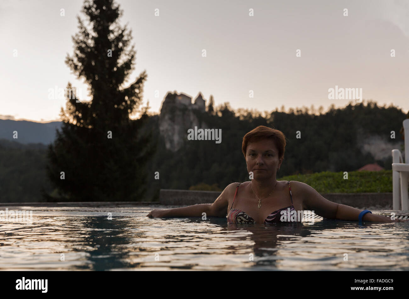 Curtido blanco mujer de mediana edad en la piscina al aire libre al atardecer. Castillo de Bled en el fondo. Eslovenia Foto de stock
