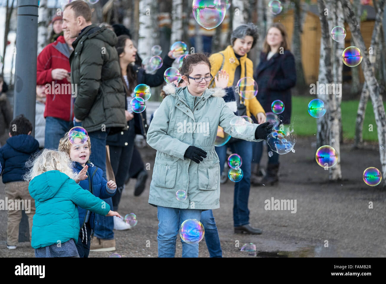 Niños entusiasmados persiguiendo burbujas creadas por un artista de la calle, en la orilla sur de Londres. Foto de stock