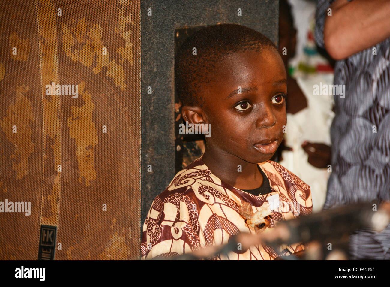 Un pequeño muchacho gambiano de pie detrás de la vieja altavoces y escuchar la música. El joven viste traje marrón de patrón. Foto de stock