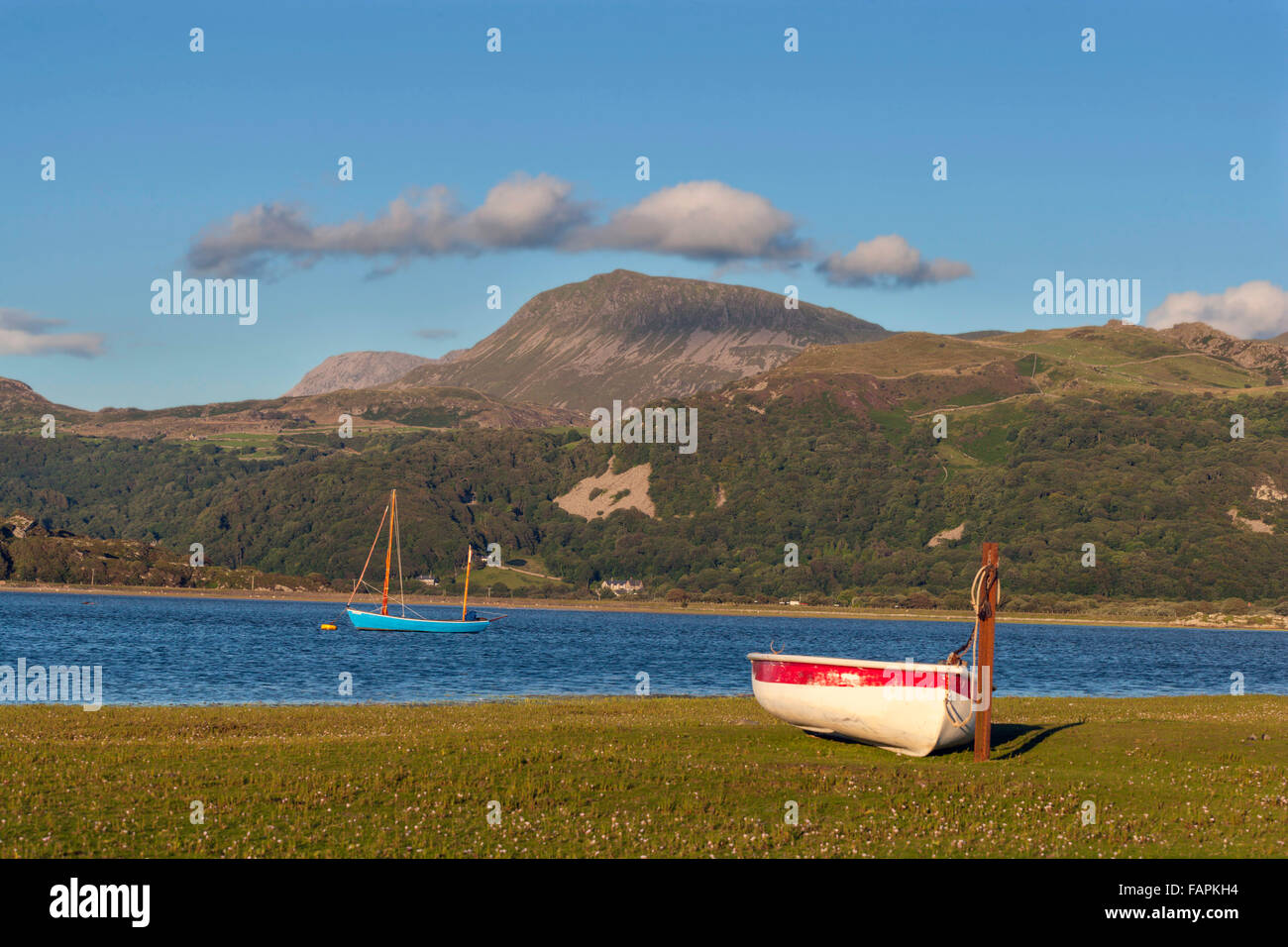 Una oferta es elaborado en el lado del estuario Mawddach con un pequeño bote de vela amarrados en el agua daba por montañas. Foto de stock