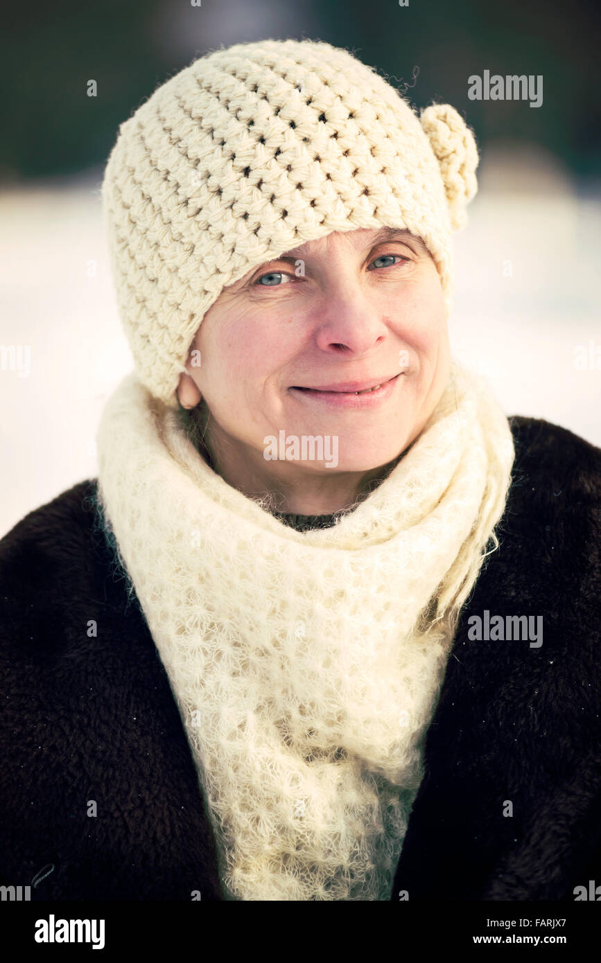 Un invierno retrato de una sonriente mujer adulta senior llevar gorro de lana y una bufanda, con un fondo de nieve Foto de stock