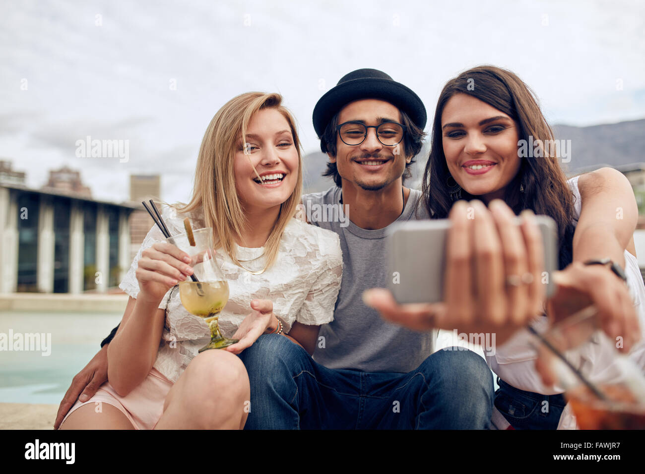 Jóvenes tomando autorretrato con teléfono inteligente durante una fiesta. Los jóvenes hombres y mujeres teniendo selfie en parte en la azotea. O colgantes Foto de stock