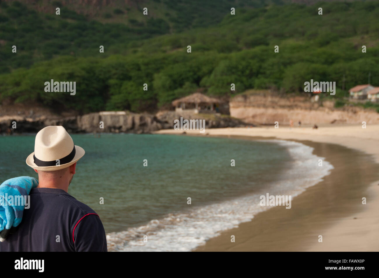 Hombre con sombrero blanco y toalla caminando solitaria playa de arena Foto de stock
