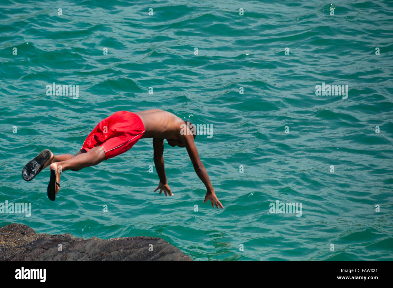 Hombre Negro con calzones rojos saltar al agua del océano Foto de stock