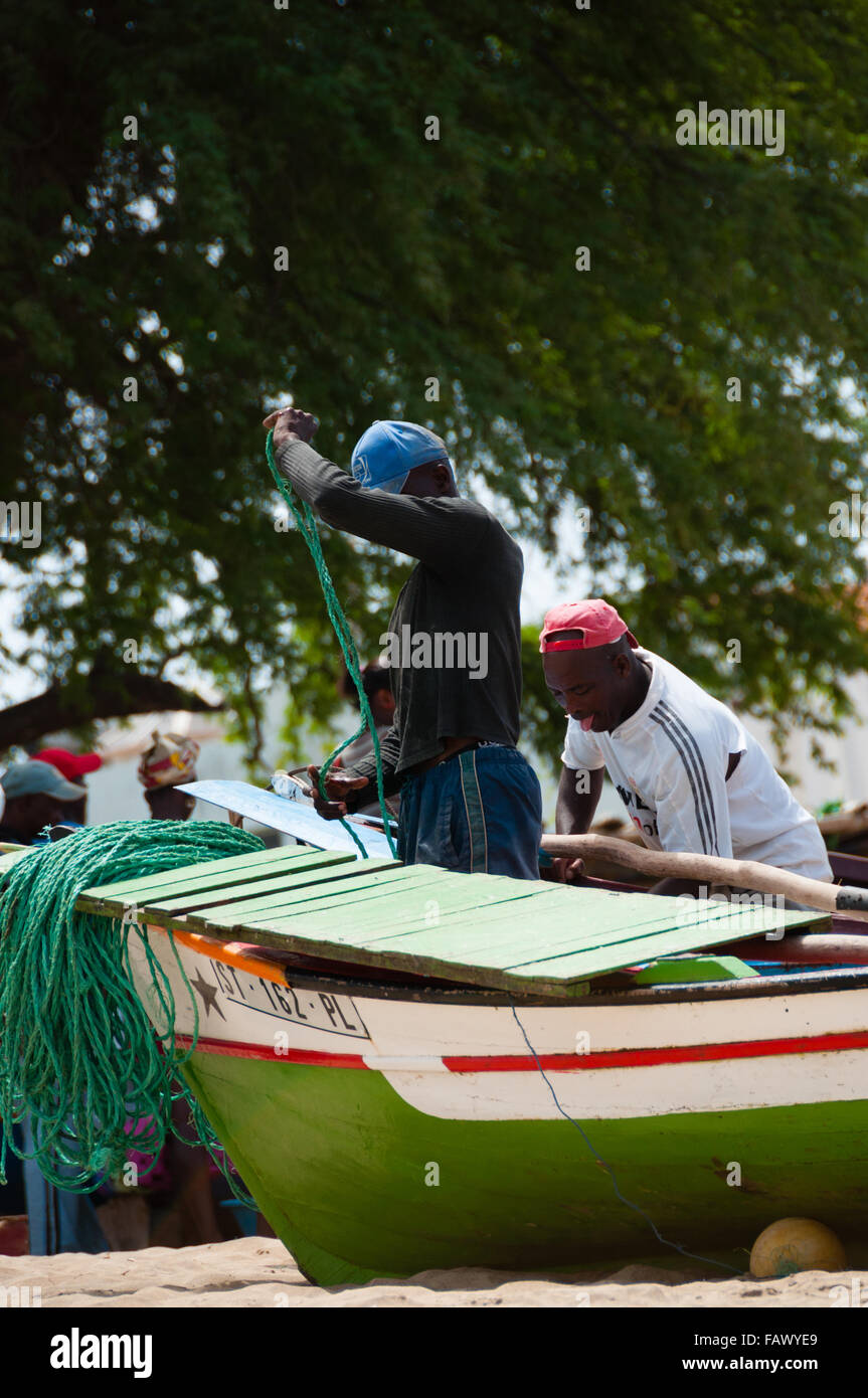 Dos pescadores africanos trabajan en la playa entre las embarcaciones con red de pesca Foto de stock