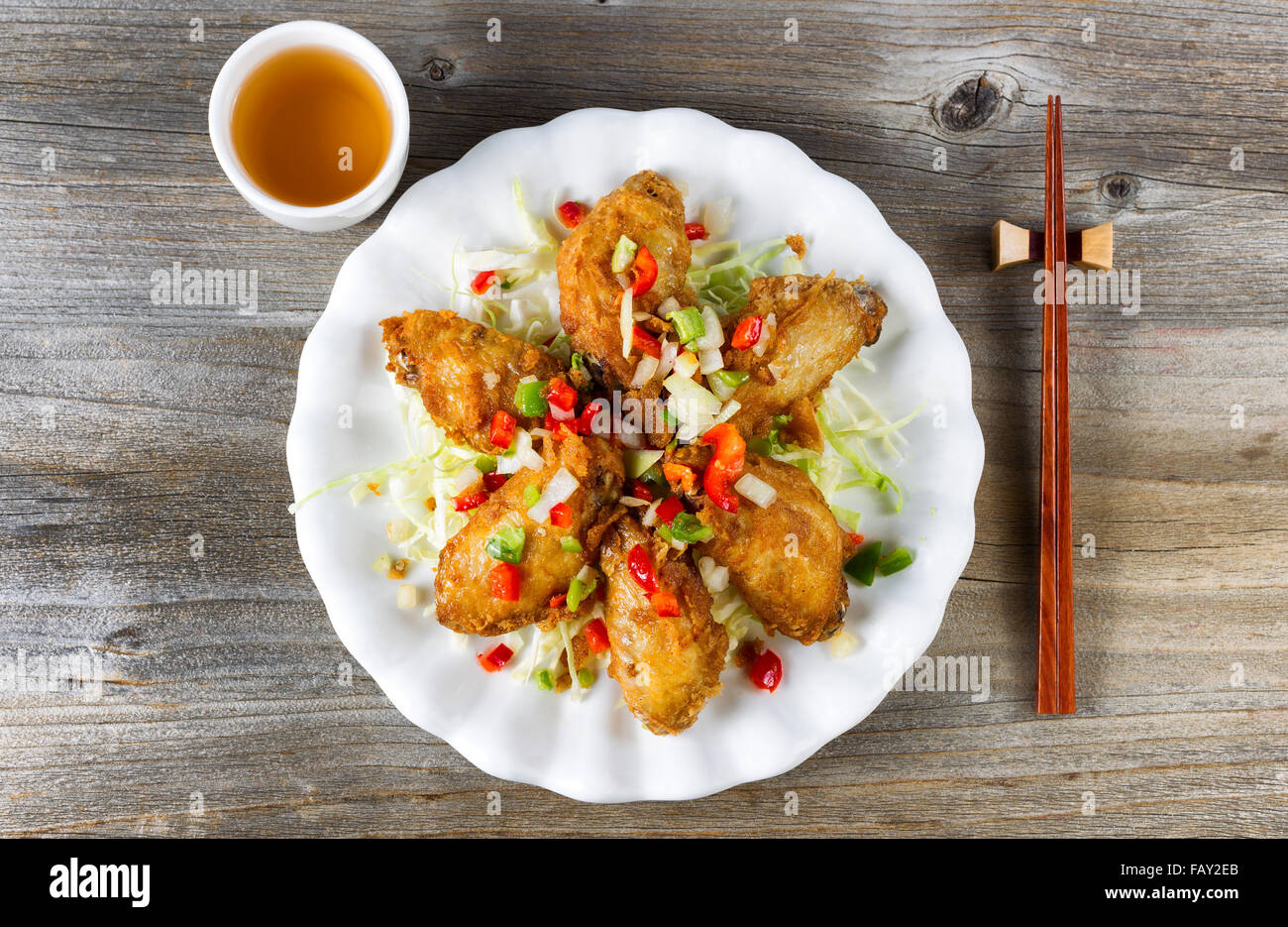 Vista superior de estilo asiático frito alitas de pollo en la placa blanca  con aderezos. El té verde y los palillos en el soporte. Boa de madera  rústica Fotografía de stock -