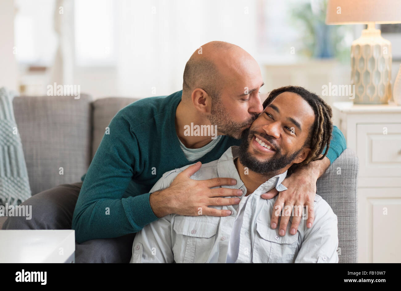 Pareja homosexual besándose por el sofá en el salón Foto de stock