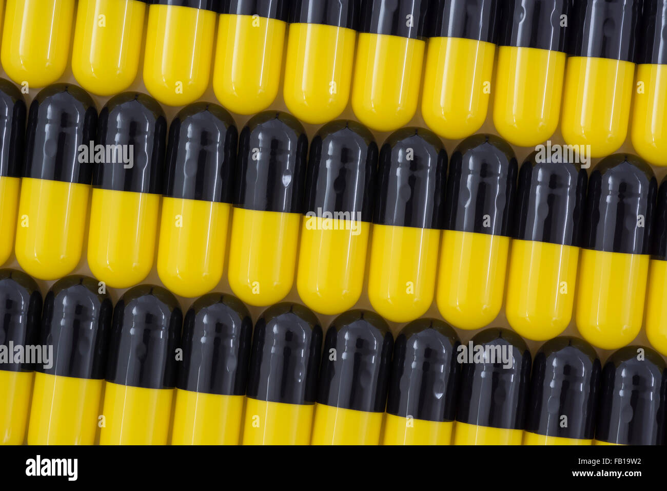 Primer plano de pastillas - forma de cápsula hecha de gelatina. Pastillas amarillas / negras. Metáfora tomando a las compañías farmacéuticas estadounidenses sobre los altos precios de los medicamentos, ensayos de drogas. Foto de stock