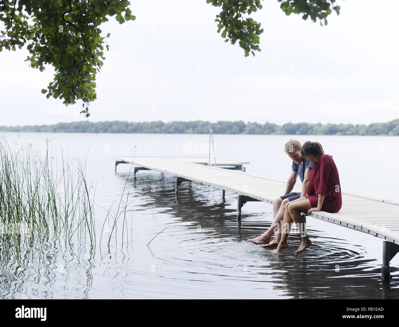 Pareja Sentada en el muelle al lado sumergir los pies en agua, Copenhague, Dinamarca Foto de stock