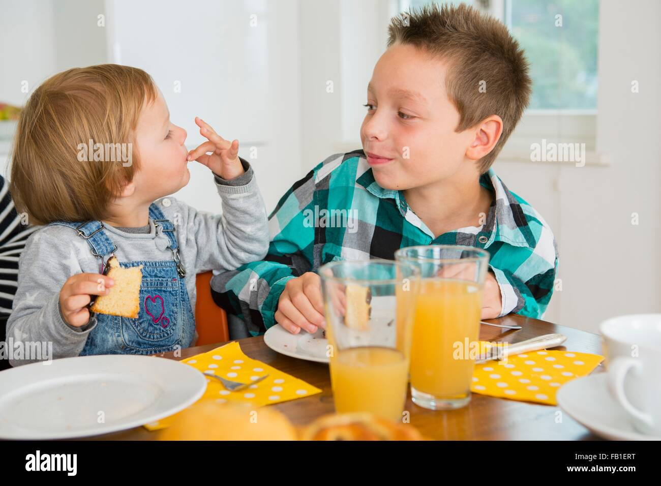 Lindo niño hembra lamer los dedos en la mesa de la cocina Foto de stock
