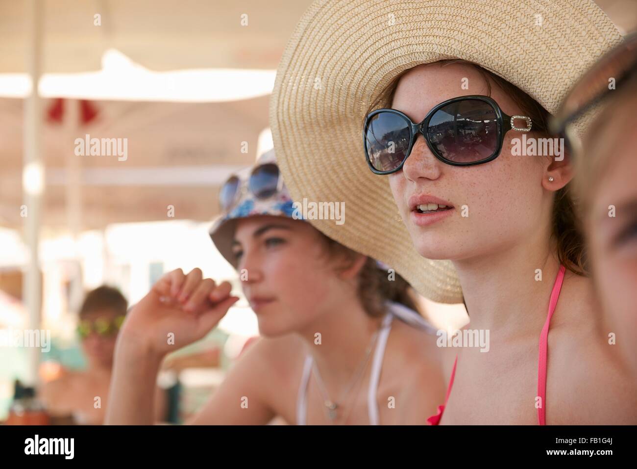 Fila de adolescentes vistiendo gorros para el sol relajarse bajo las sombrillas Foto de stock