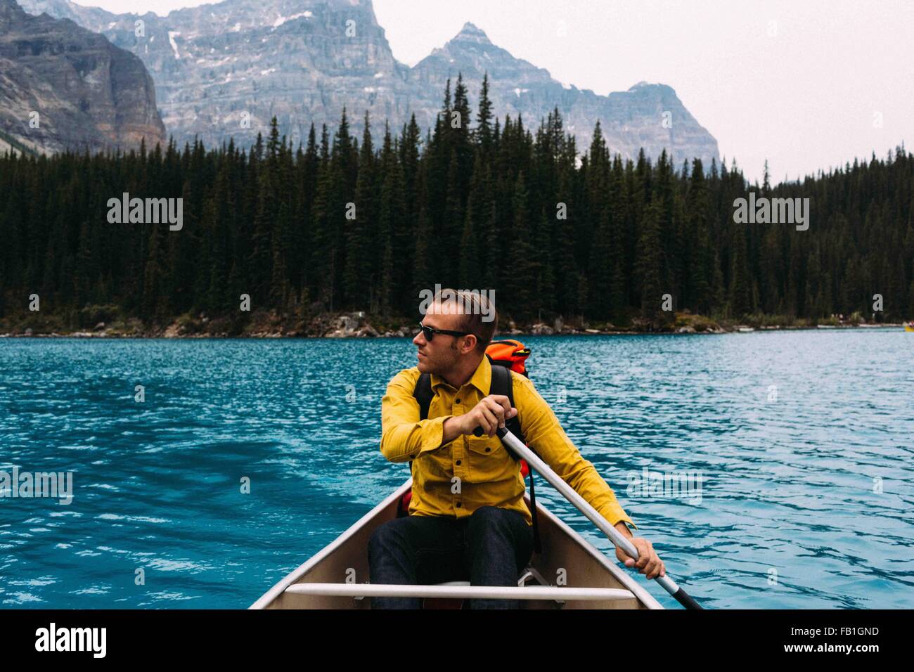 Vista frontal de mediados del hombre adulto, remar en canoa, apartar la mirada, el lago Moraine, el Parque Nacional de Banff, Alberta, Canadá Foto de stock