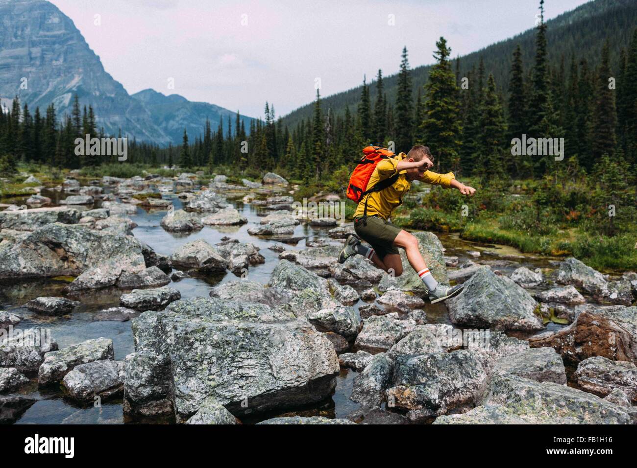 Vista lateral de un hombre adulto medio llevar mochila saltar más pedregoso cauce, el lago Moraine, el Parque Nacional de Banff, Alberta, Canadá Foto de stock