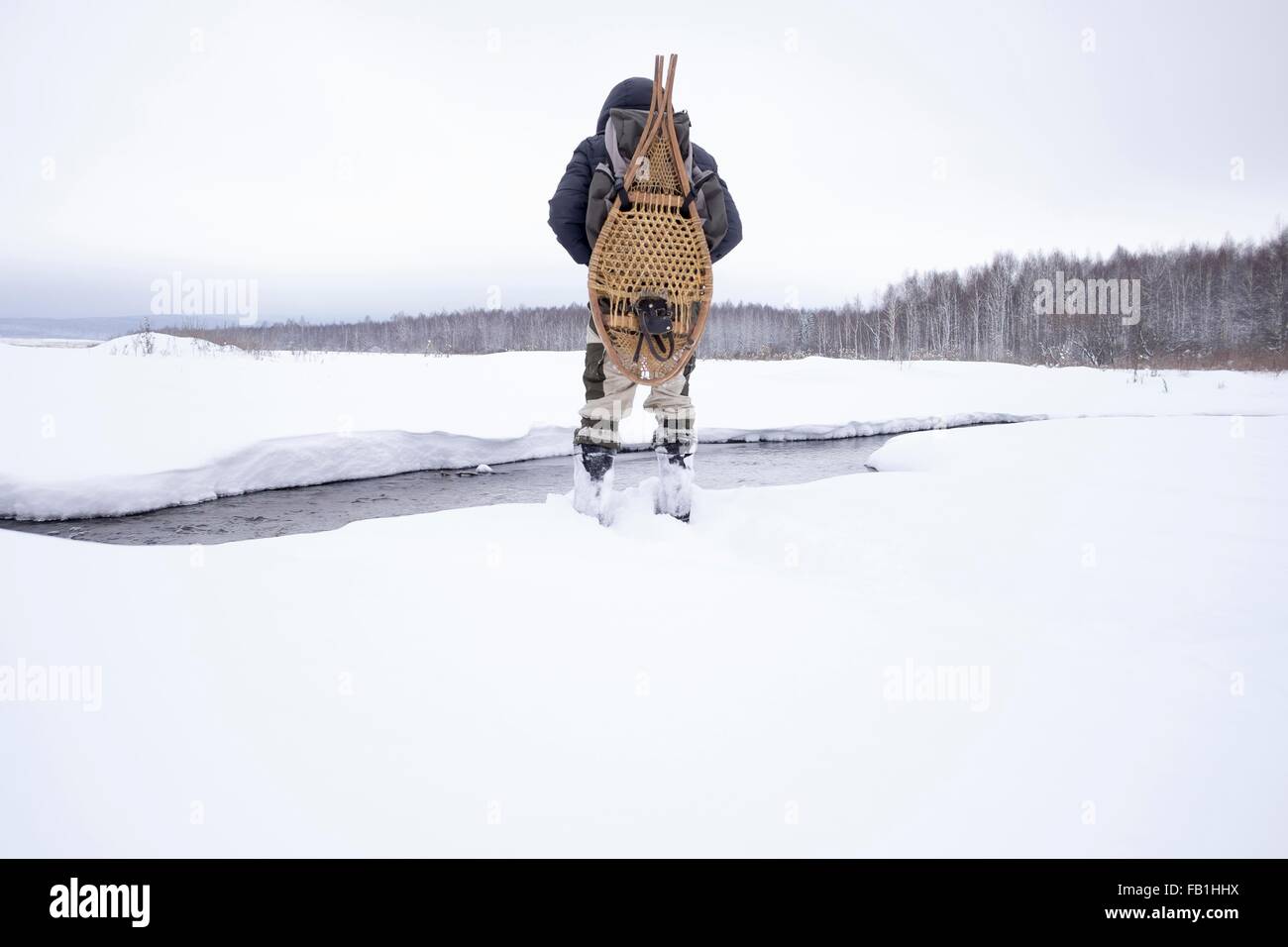 Vista trasera de mediados del hombre adulto en el campo cubierto de nieve por río llevando raquetas tradicionales, Ural, Rusia Foto de stock