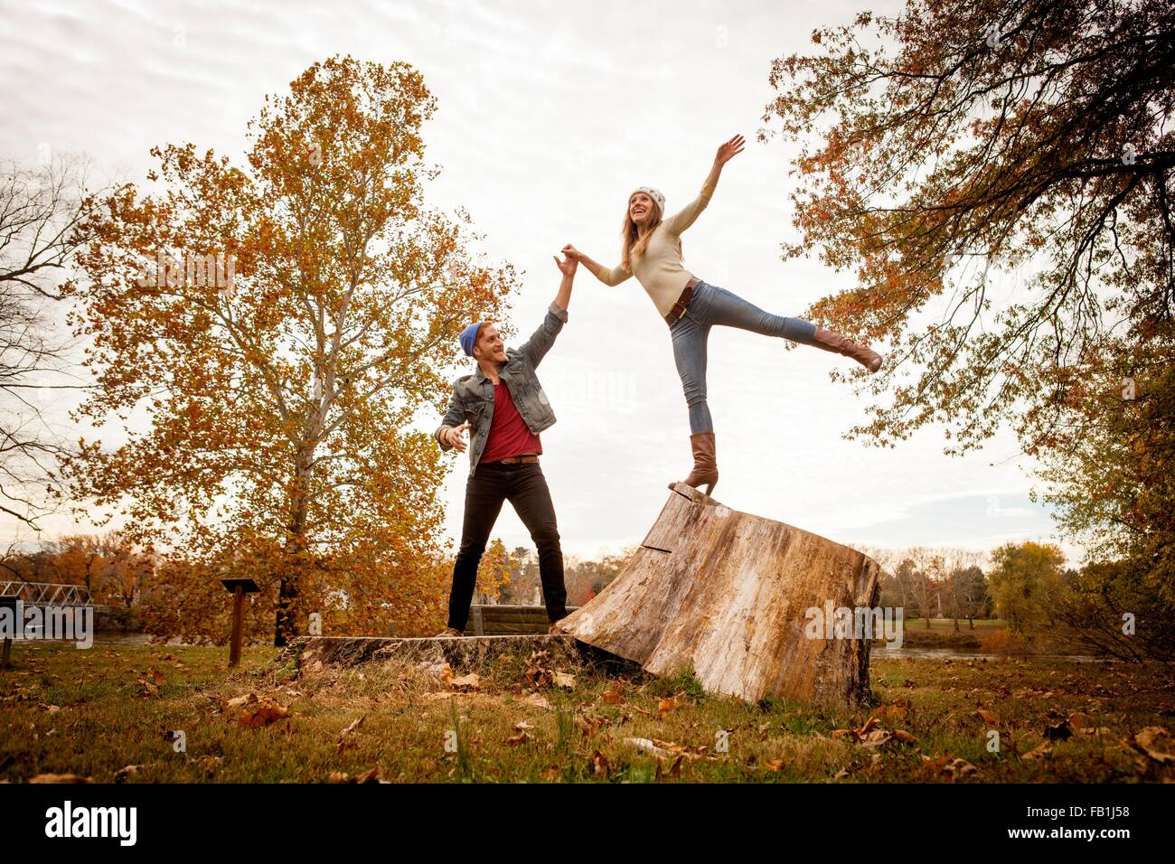 Pareja joven jugando en tocón de árbol en otoño park Foto de stock