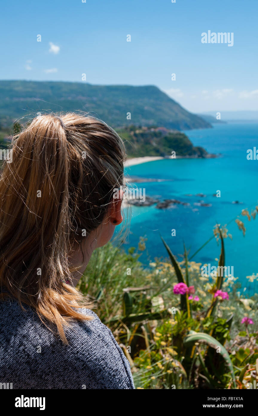 Mujer rubia desde detrás buscando más hermosas de la costa de Calabria, frente al azul mar mediterráneo Foto de stock