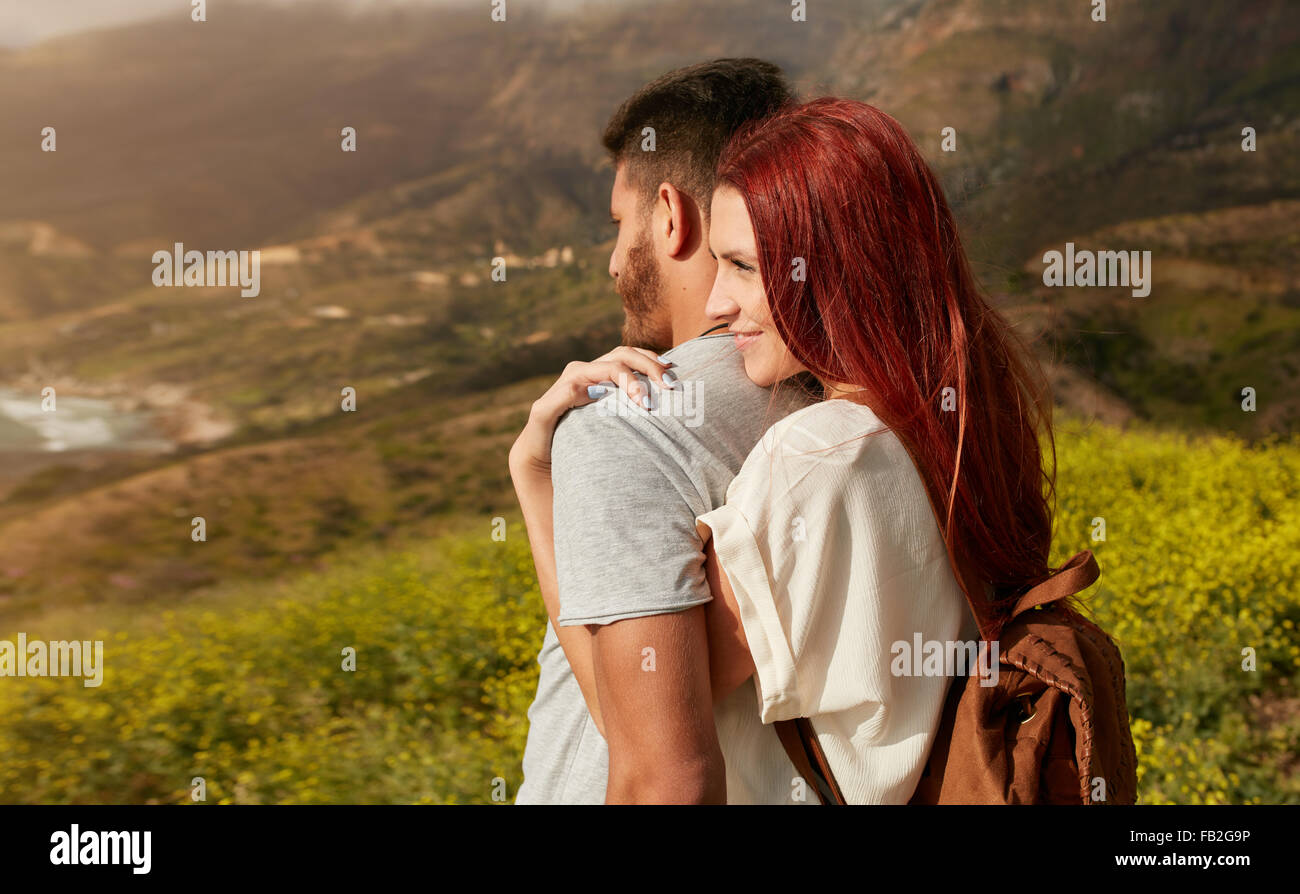 Romántica pareja joven disfruta de las vistas mientras senderismo por la montaña. Mujer joven abrazando a su novio desde detrás, WH Foto de stock