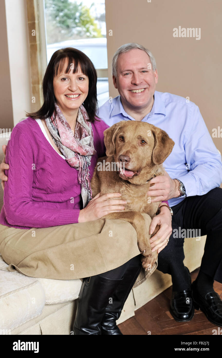 Una pareja de mediana edad sentado en un sofá abrazando a su perro Foto de stock