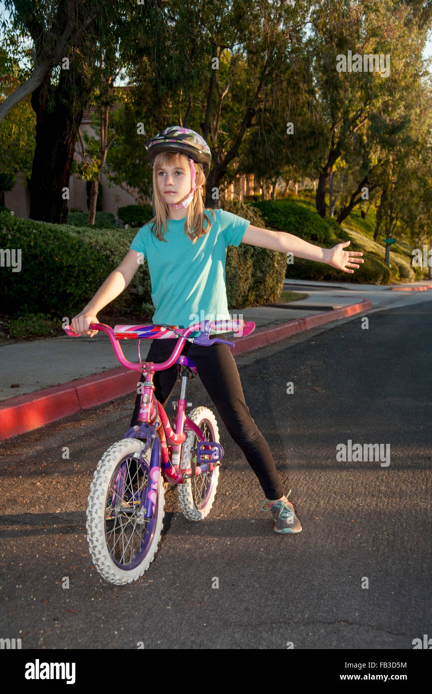 Una interpolación chica ciclista indica un giro a la izquierda con su brazo en una calle en Lake Forest, CA MODELO DE LIBERACIÓN Foto de stock