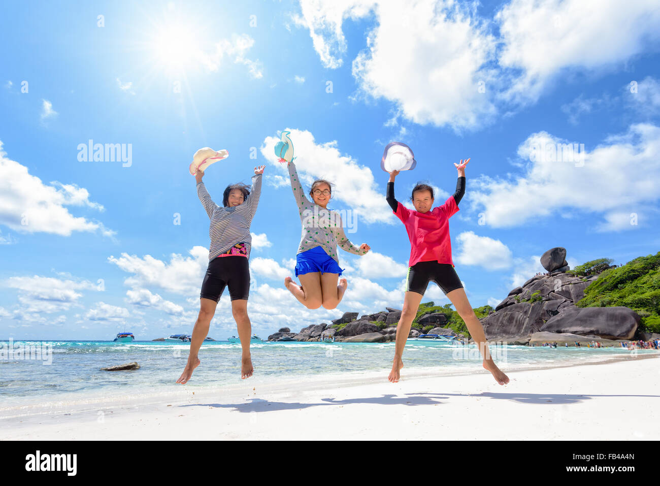 Las mujeres de tres generaciones de la familia turística brincar de feliz en la playa cerca del mar bajo el cielo de nubes y el sol de verano en Similan Foto de stock