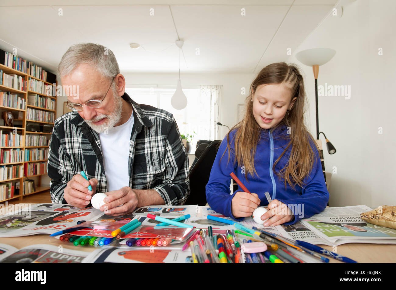 Suecia, Chica (10-11) con el abuelo colorear huevos en el salón Foto de stock