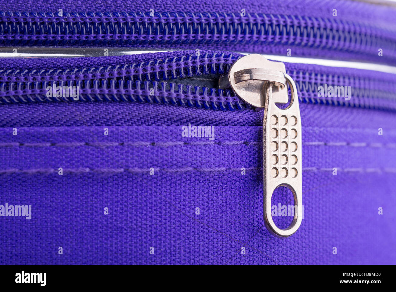 Macro de una cremallera mostrando la lengüeta y la cadena en una maleta violeta listo para un seguro de viaje de vacaciones Foto de stock