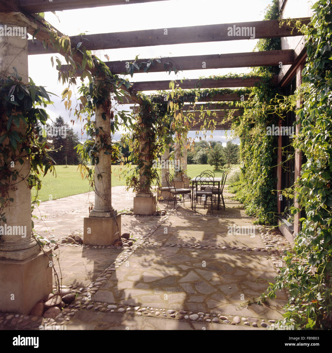 Pérgola de madera y piedra encima pavimentado patio con muebles de metal  verde y plantas trepadoras en un país grande jardín Fotografía de stock -  Alamy