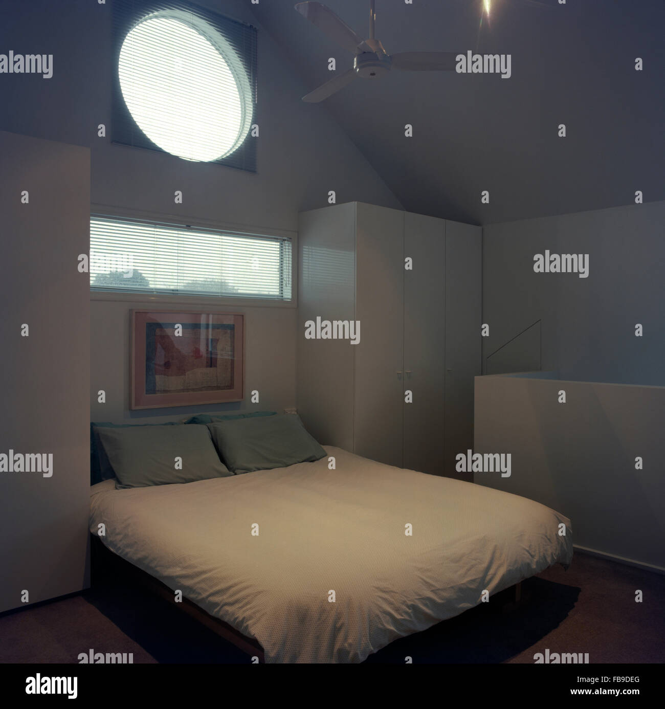 Ventanas circulares y rectangulares encima de la cama con edredón blanco en 90 dormitorio Foto de stock