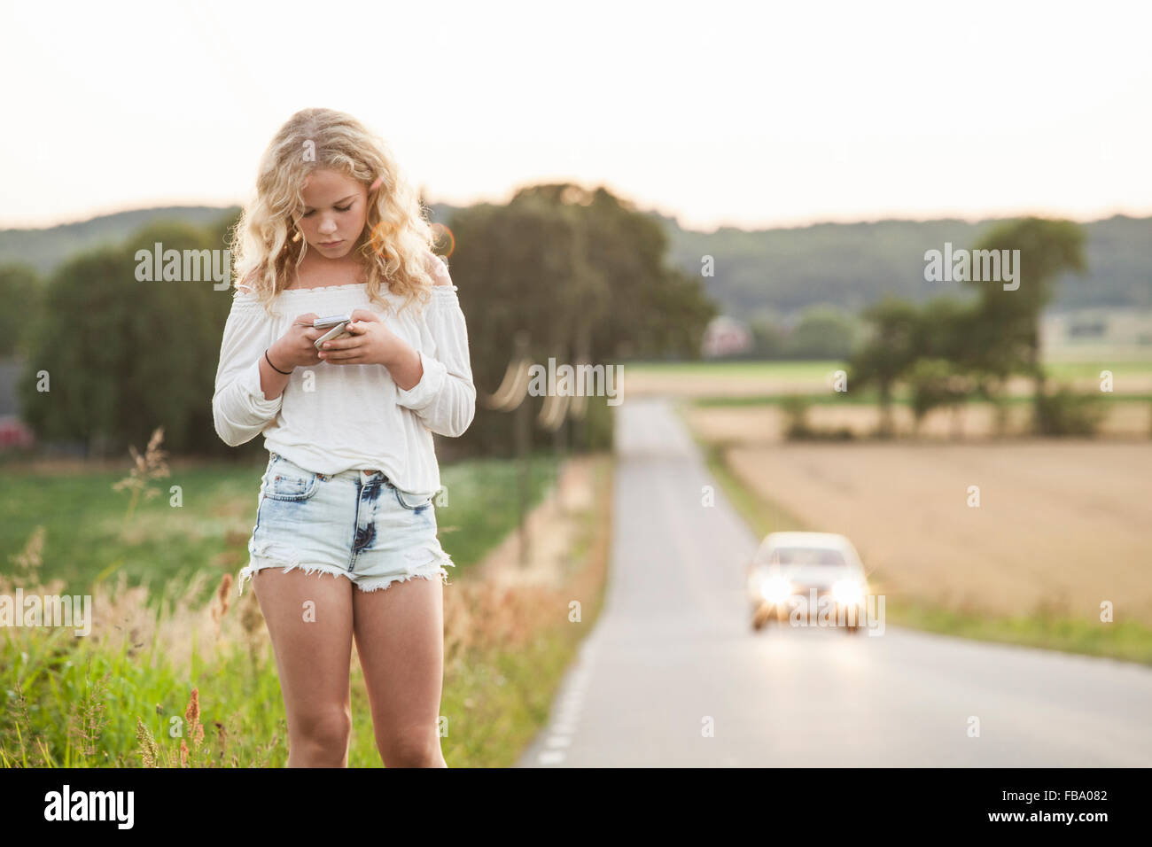 Suecia, Blekinge, Solvesborg, adolescente (14-15) con el teléfono móvil de pie al lado de la carretera Foto de stock