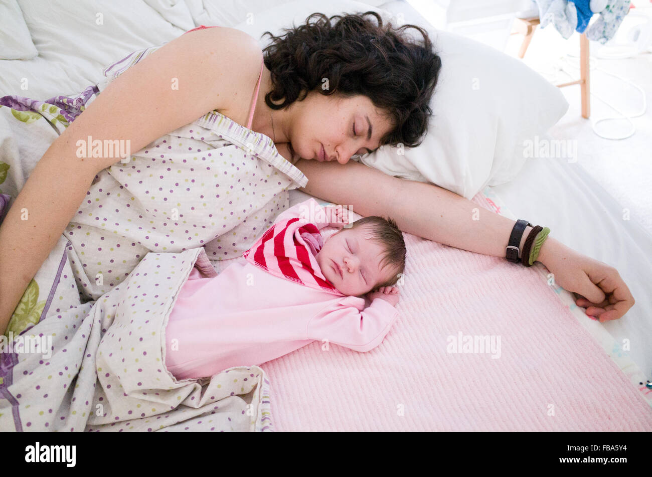 La madre durmiendo con su bebé recién nacido junto a ella en la misma cama Foto de stock