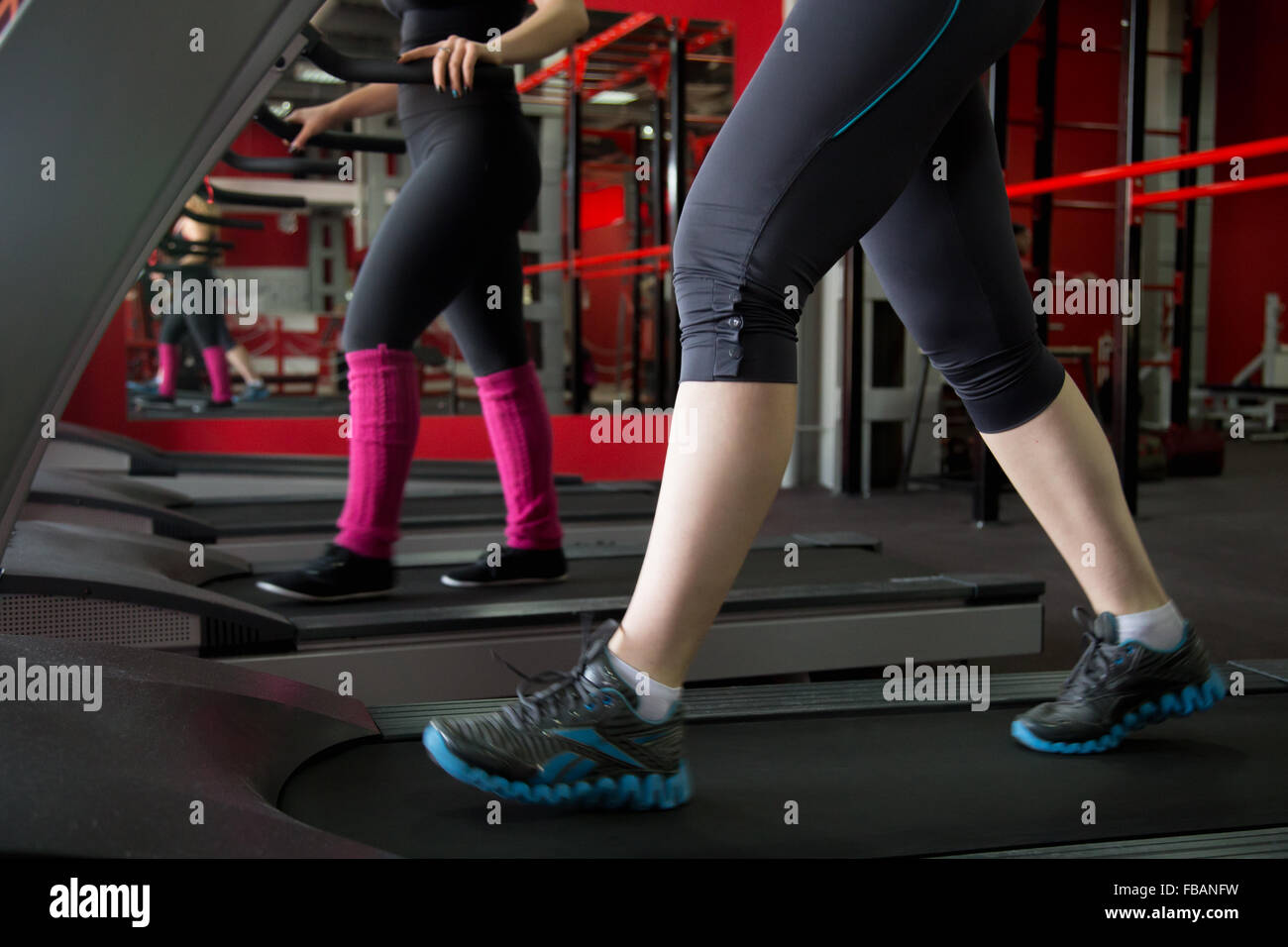 Dos niñas en zapatillas se ejecutan en cardio trainer, cinta de correr en el gimnasio (vista desde el sneakers) Foto de stock